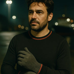 Man wearing a black sweater and red pants with gloves in a dark, possibly urban setting.