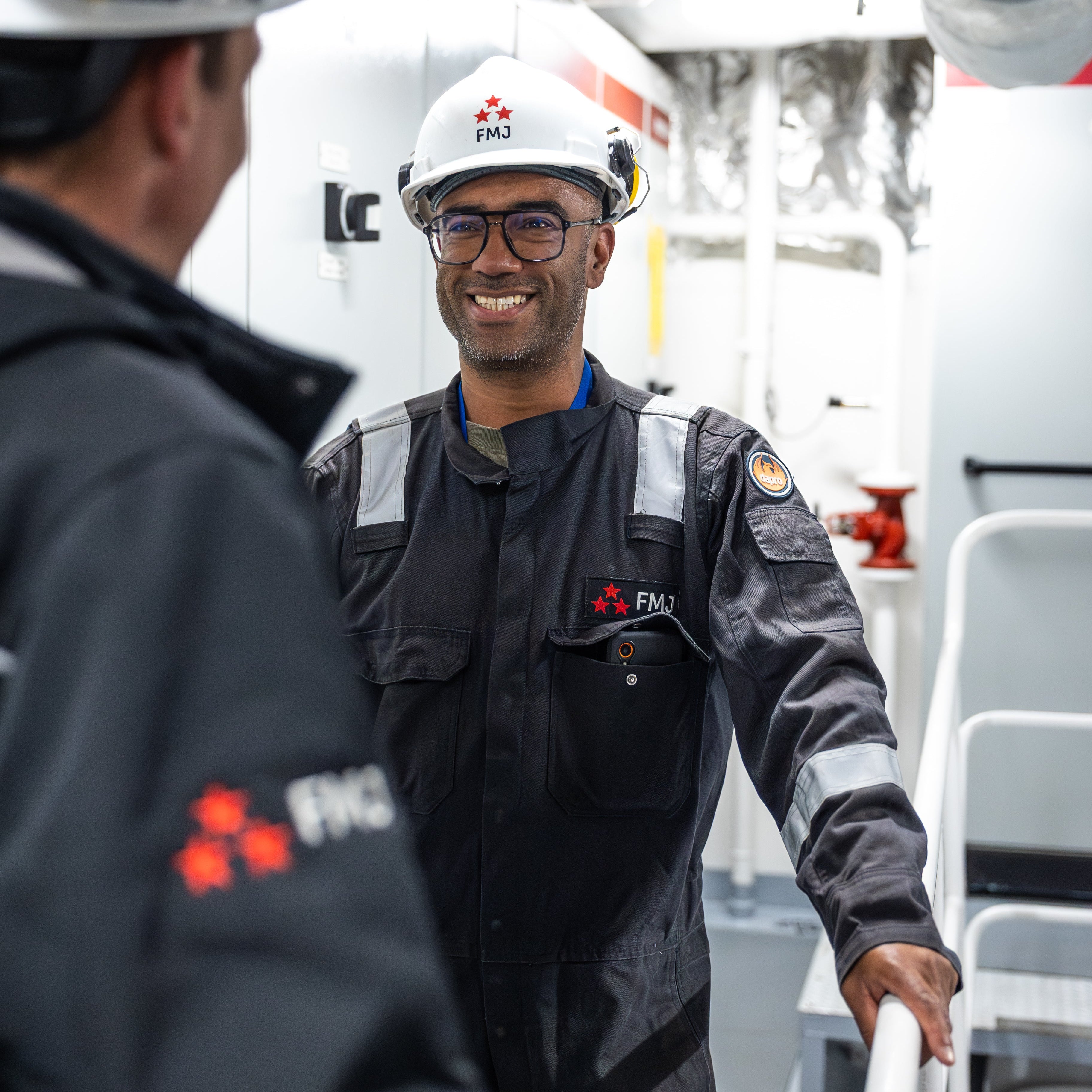 Two individuals in safety gear with visible branding in an industrial setting